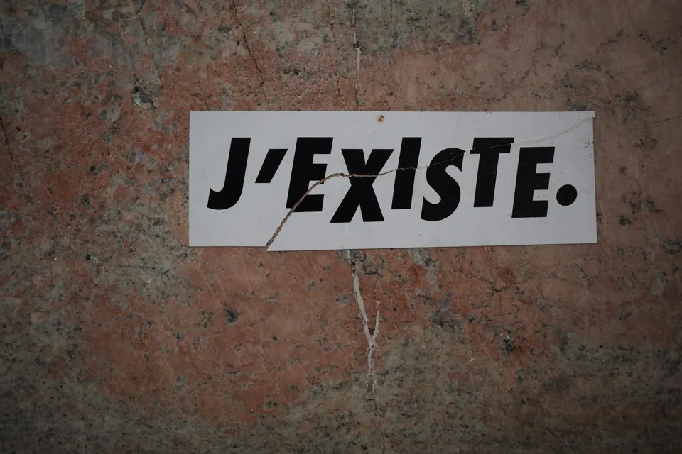 Cartaz com a frase J'existe (eu existo) colado num muro
