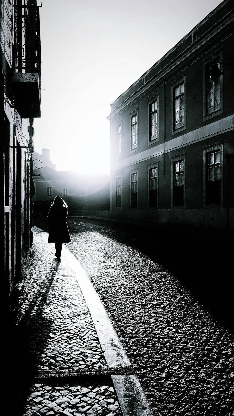 Pessoa caminhando sozinha numa rua de pedra, contra a luz